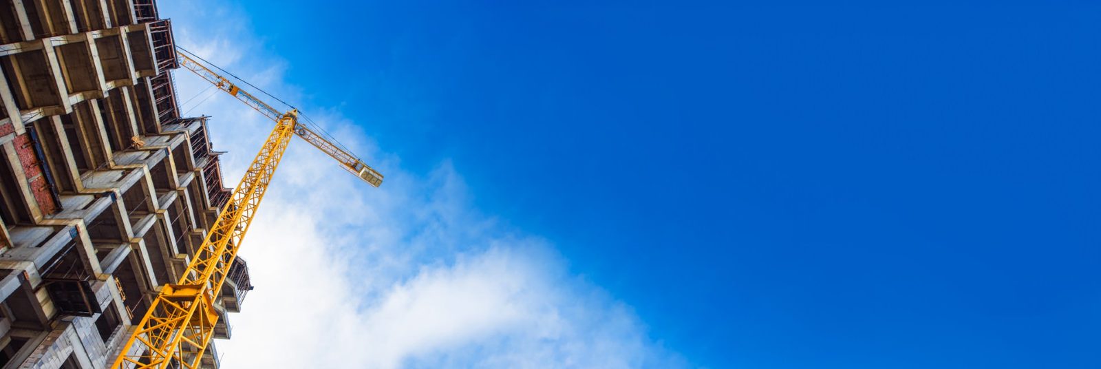 Tower crane rising over a concrete building frame against a blue sky